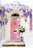 This image presents a graceful Millbank entrance, styled as if to welcome someone home for the very first time. At the centre, a softly painted pink front door stands against whitewashed walls, its pastel tone lending a tender warmth to the scene. A matching shutter, also in blush, reinforces the serene colour palette and hints at the quiet charm of the streets that weave between Millbank and nearby Westminster. Above and around the door, wisteria cascades in lavish drapes, its blossoms forming trails of lavender and pale purple that hang like delicate, perfumed curtains. The floral clusters are full yet airy, and occasional strands of fresh greenery tuck in among the petals, suggesting a living, breathing canopy. On the doorstep, a sturdy grey bucket has been placed with intention, acting as a simple vessel for a luxurious cluster of white and cream roses. The roses are large and generously open, each flower layered with countless soft petals that create a sense of fullness and comfort. Between them, small tufts of green foliage add contrast and shape without disturbing the soothing palette. Encircling the base of the bucket is a pink ribbon tied in a loose, romantic bow, repeating the pink tones of the door and visually stitching the whole arrangement together. The overall light is calm and flattering, suggesting a peaceful afternoon when the city slows just a little. The entire composition feels like a thoughtfully prepared housewarming gift from Flowers Millbank, celebrating a new address with understated elegance, floral fragrance, and the quiet promise that this doorway will soon be crossed by friends, family, and happy everyday moments.